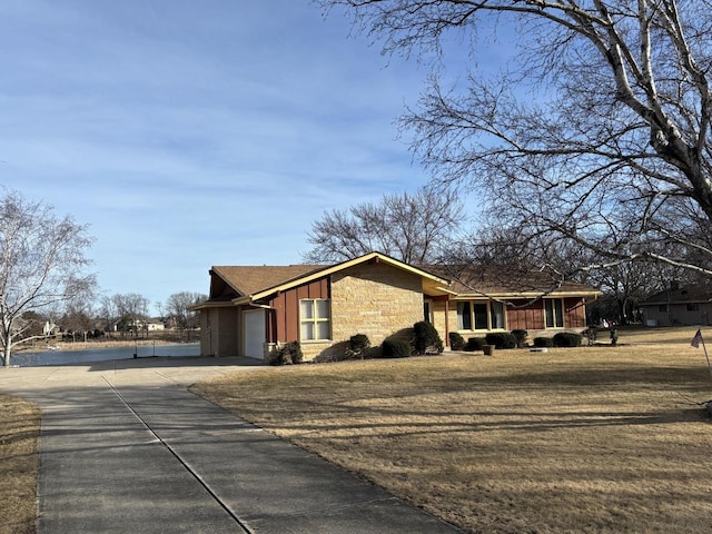 view of side of home with board and batten siding, concrete driveway, a yard, a garage, and stone siding