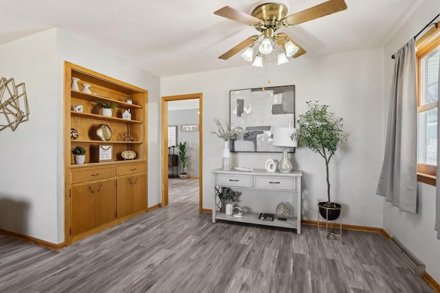 interior space with ceiling fan, built in shelves, baseboards, and wood finished floors