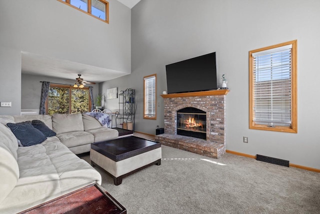 carpeted living area with visible vents, baseboards, a fireplace, a towering ceiling, and a ceiling fan