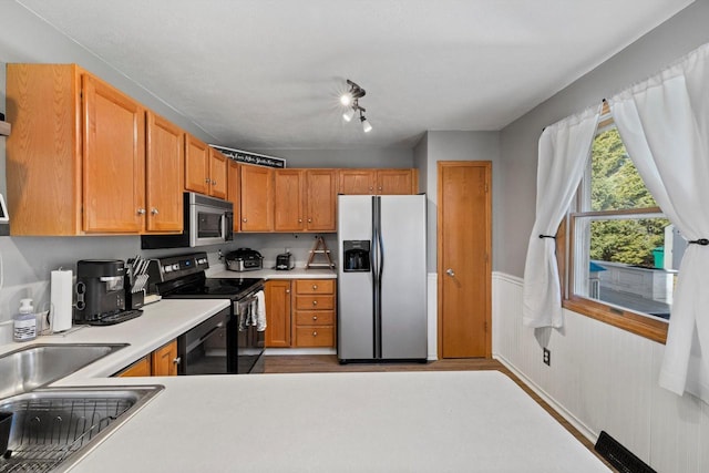 kitchen featuring a sink, stainless steel appliances, a wainscoted wall, and light countertops