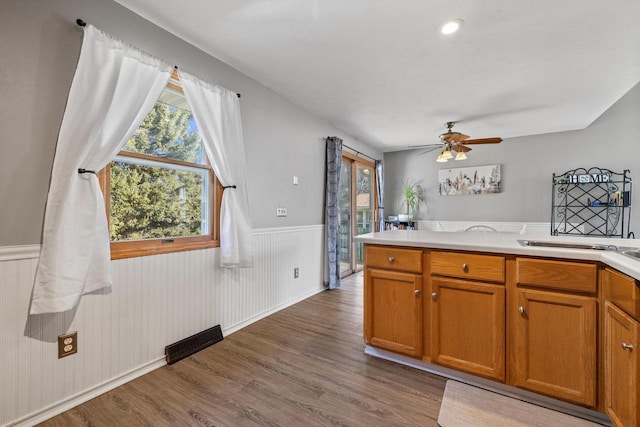 kitchen featuring brown cabinetry, a wainscoted wall, wood finished floors, visible vents, and light countertops