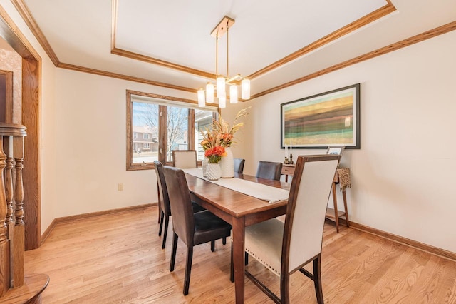 dining space with a raised ceiling, light wood-style floors, baseboards, and ornamental molding