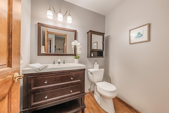 half bathroom featuring toilet, vanity, baseboards, and wood finished floors