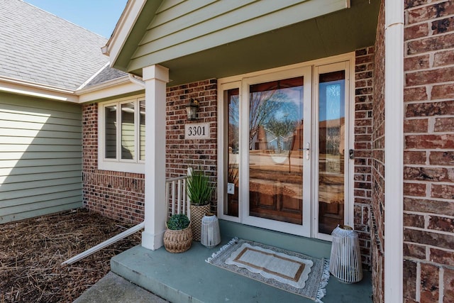 property entrance featuring brick siding, a porch, and a shingled roof