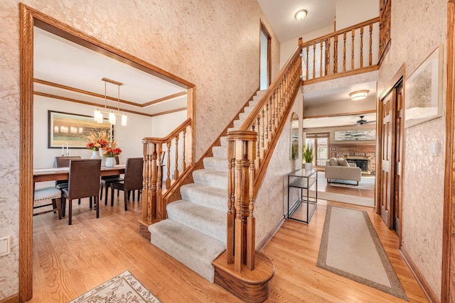 staircase with wood finished floors, crown molding, a fireplace with raised hearth, and a towering ceiling