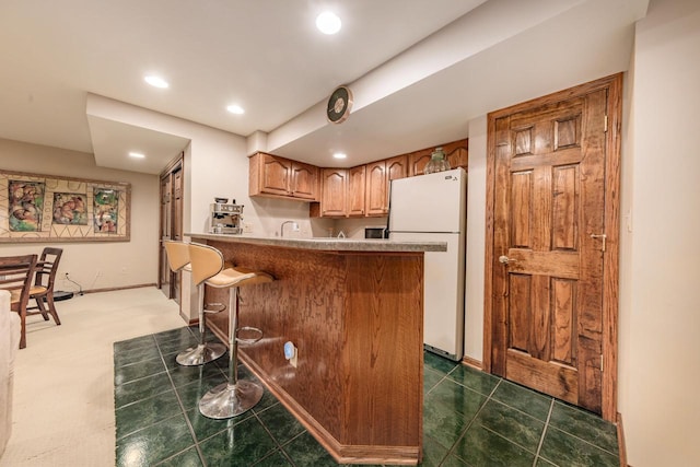 kitchen featuring a breakfast bar, a peninsula, recessed lighting, freestanding refrigerator, and a sink