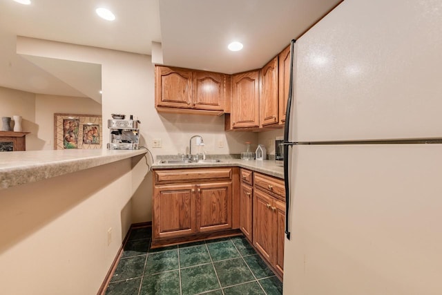 kitchen featuring dark tile patterned floors, brown cabinets, freestanding refrigerator, and a sink