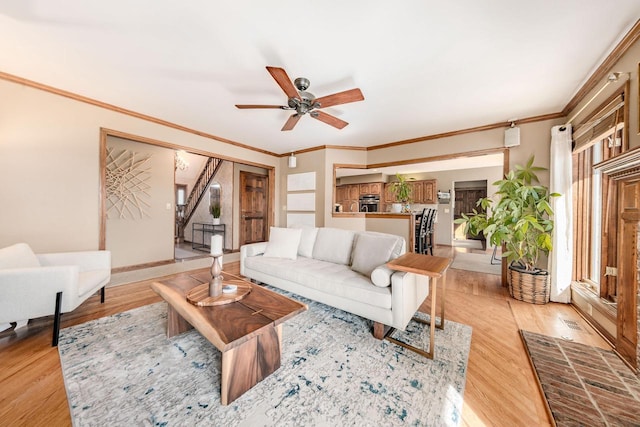 living room featuring ceiling fan, baseboards, light wood-style floors, and ornamental molding