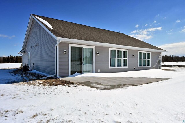 snow covered house with central air condition unit and roof with shingles