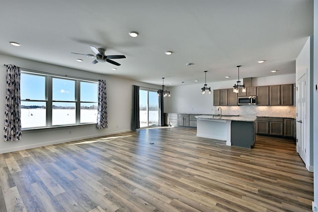 kitchen with a kitchen island with sink, stainless steel microwave, open floor plan, and dark wood-style flooring