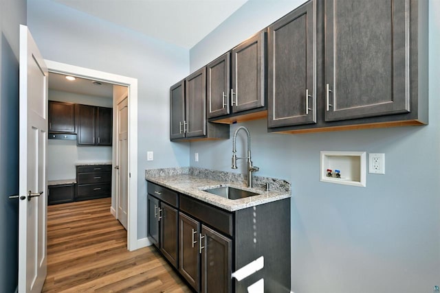 kitchen featuring a sink, wood finished floors, baseboards, dark brown cabinets, and light stone countertops