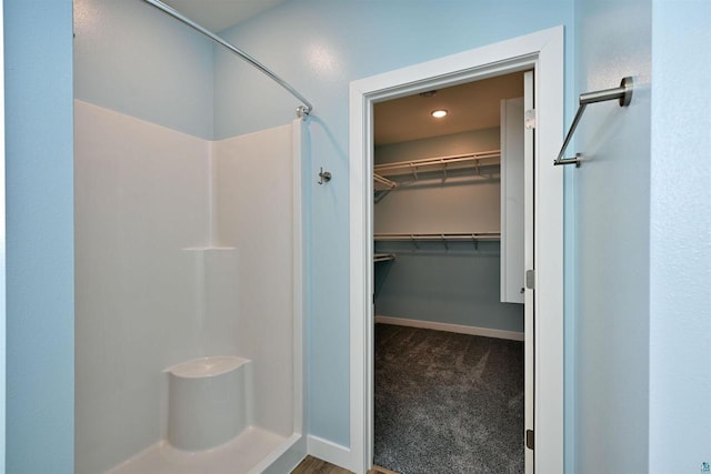 bathroom featuring a spacious closet, baseboards, and a stall shower