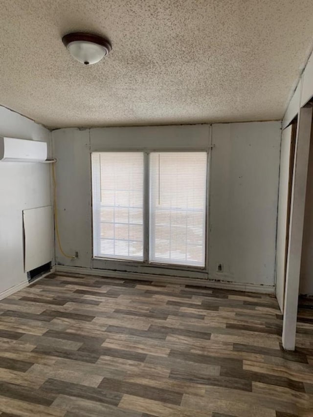 unfurnished room with a textured ceiling, dark wood-type flooring, and a wall unit AC