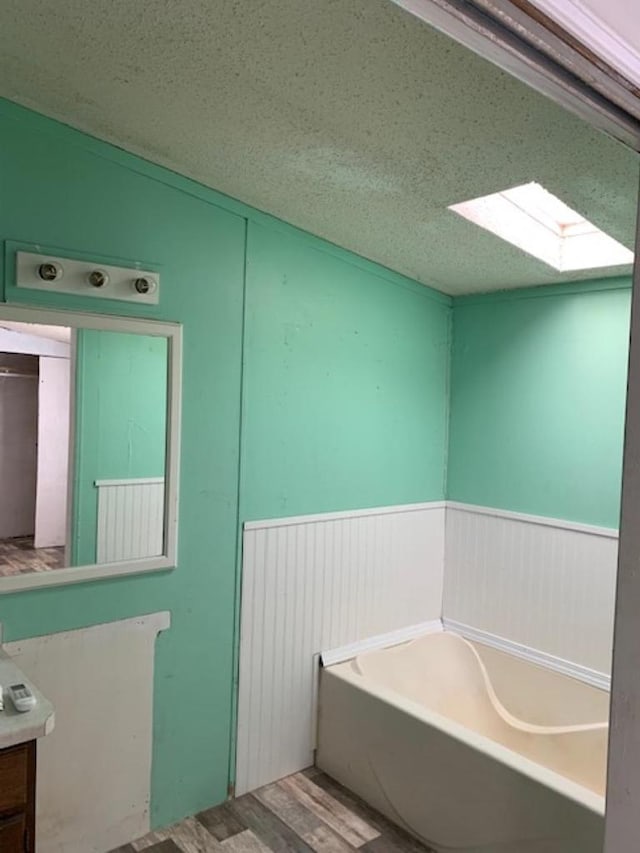 bathroom featuring vanity, wood finished floors, wainscoting, a textured ceiling, and a garden tub