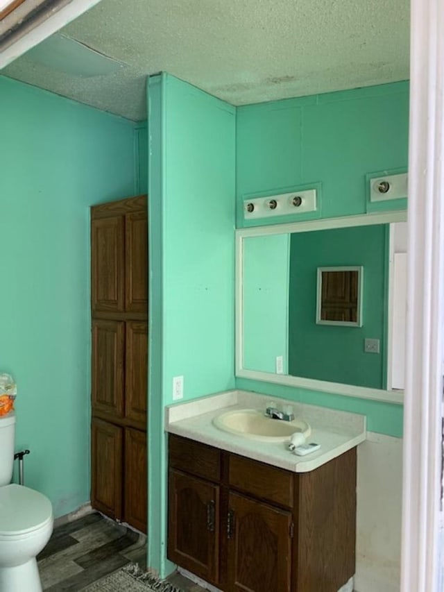 bathroom with vanity, toilet, wood finished floors, and a textured ceiling