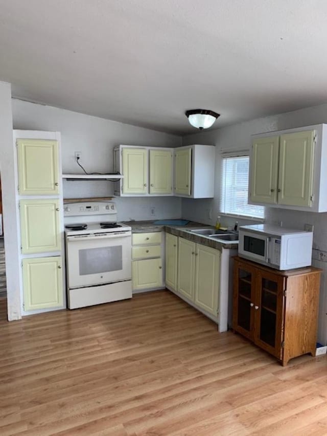 kitchen with white appliances, green cabinetry, a sink, dark countertops, and light wood-type flooring