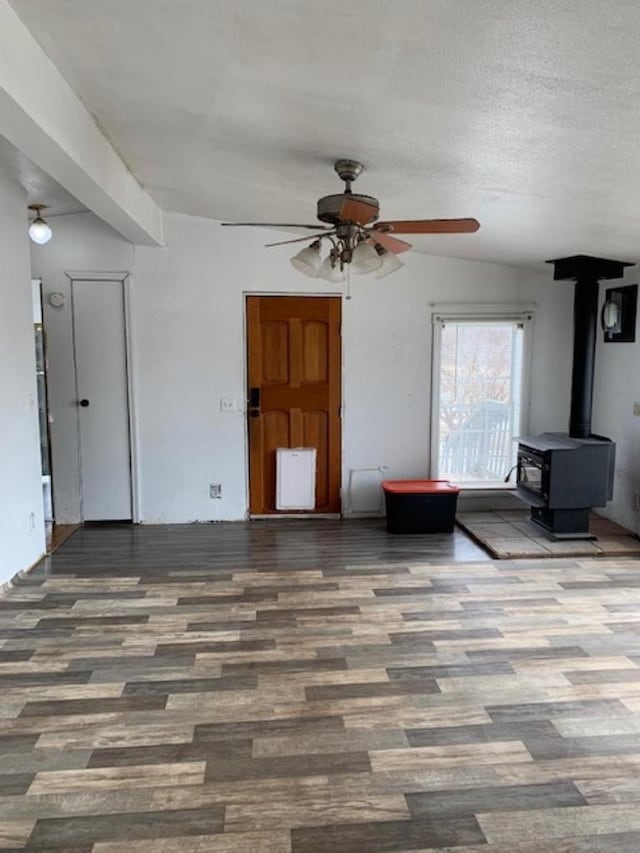 unfurnished living room with a textured ceiling, a wood stove, ceiling fan, and wood finished floors