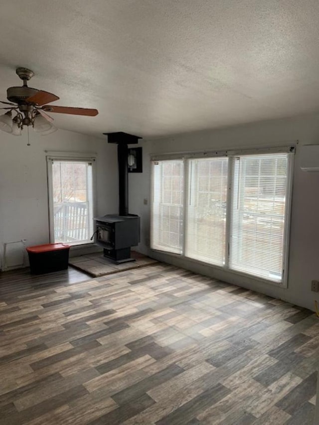 unfurnished living room featuring a wood stove, wood finished floors, and a textured ceiling