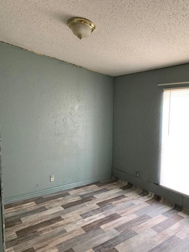 spare room with baseboards, a textured ceiling, wood finished floors, and a textured wall