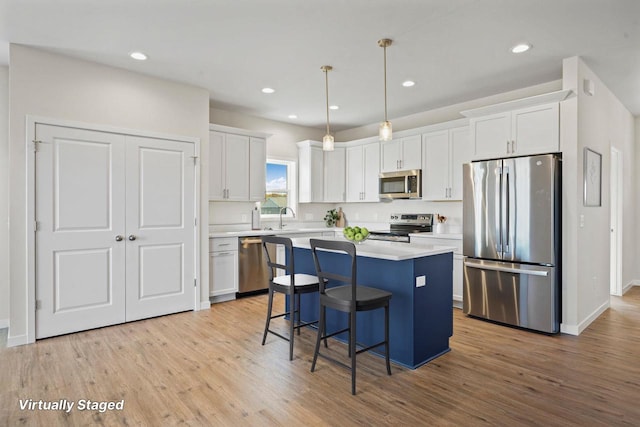 kitchen with light wood-style flooring, a kitchen island, appliances with stainless steel finishes, and white cabinets