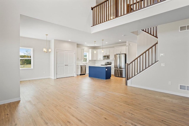 unfurnished living room with light wood finished floors, visible vents, a high ceiling, and baseboards