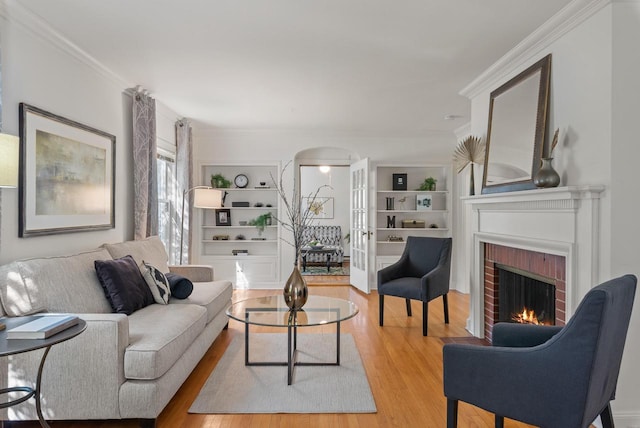 living room featuring arched walkways, a brick fireplace, wood finished floors, and crown molding