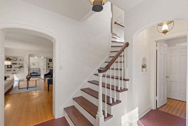stairway featuring arched walkways, baseboards, and brick floor