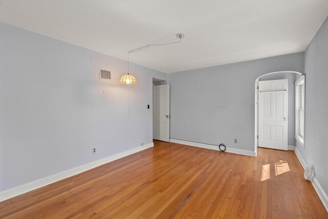 spare room featuring visible vents, baseboards, arched walkways, and light wood-style flooring