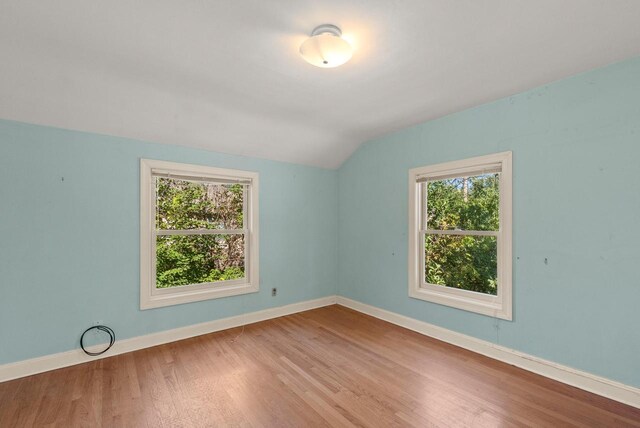 empty room with a wealth of natural light, vaulted ceiling, baseboards, and wood finished floors