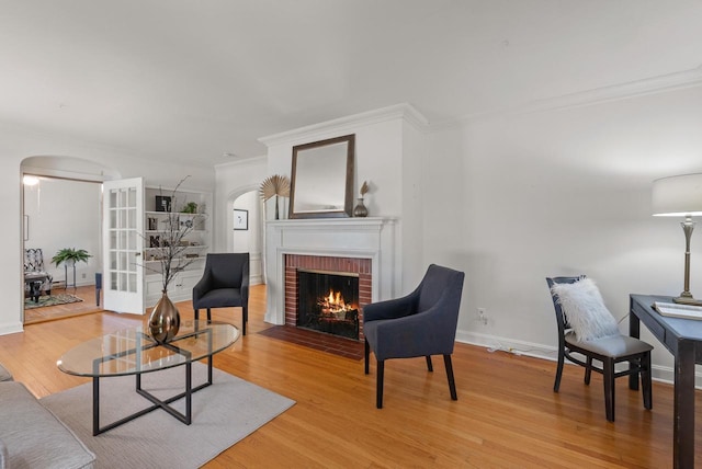 living area with arched walkways, a brick fireplace, wood finished floors, and ornamental molding