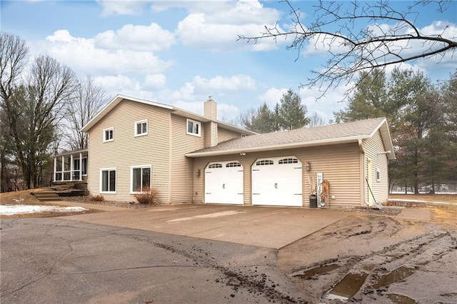 view of home's exterior with concrete driveway, a garage, a sunroom, and a chimney