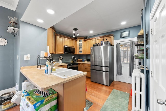 kitchen featuring glass insert cabinets, appliances with stainless steel finishes, a peninsula, light wood-style floors, and a sink