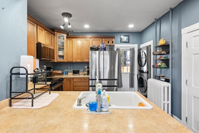 kitchen featuring stacked washer and clothes dryer, radiator, appliances with stainless steel finishes, light countertops, and glass insert cabinets