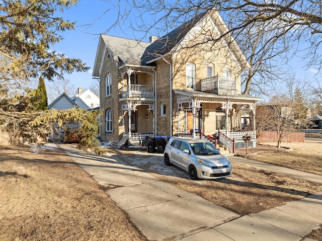 view of front facade featuring a balcony, a chimney, covered porch, and brick siding