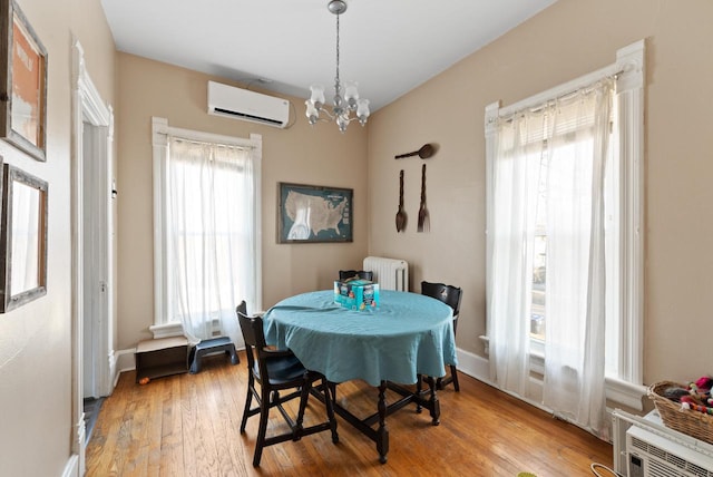 dining area with wood finished floors, baseboards, radiator heating unit, a wall mounted air conditioner, and a notable chandelier