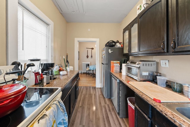 kitchen featuring radiator heating unit, freestanding refrigerator, light wood-style floors, a toaster, and dark brown cabinets