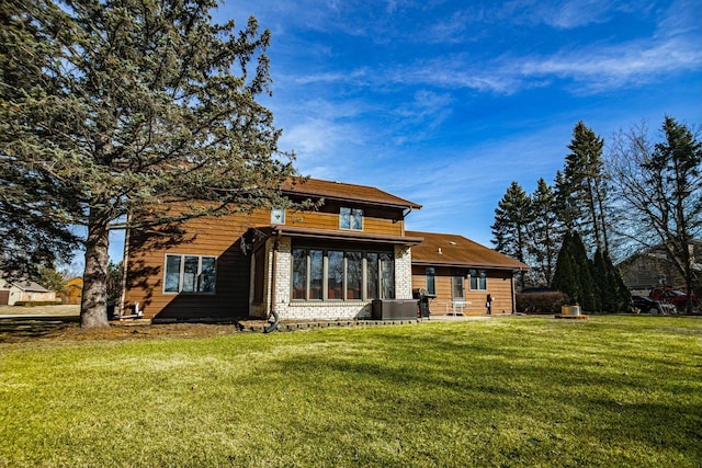 rear view of house with brick siding, a yard, and a sunroom