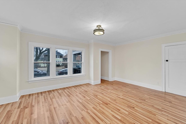 spare room featuring light wood finished floors, crown molding, and baseboards