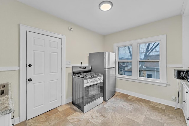 kitchen with stone finish flooring, baseboards, appliances with stainless steel finishes, and white cabinetry