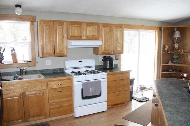 kitchen featuring light wood finished floors, dark countertops, white gas range, exhaust hood, and a sink