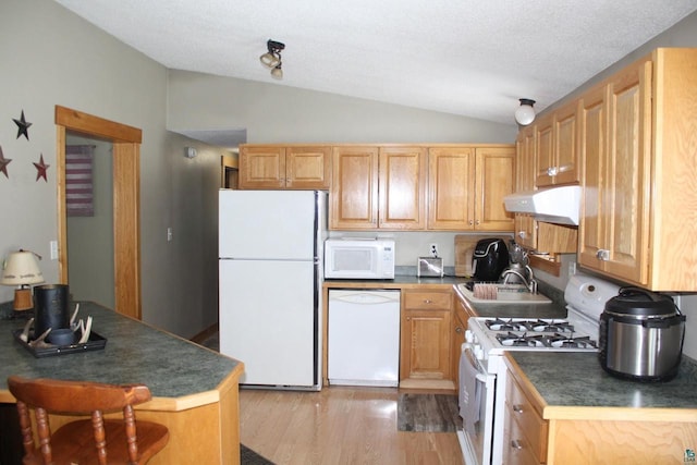 kitchen with under cabinet range hood, a sink, dark countertops, white appliances, and lofted ceiling