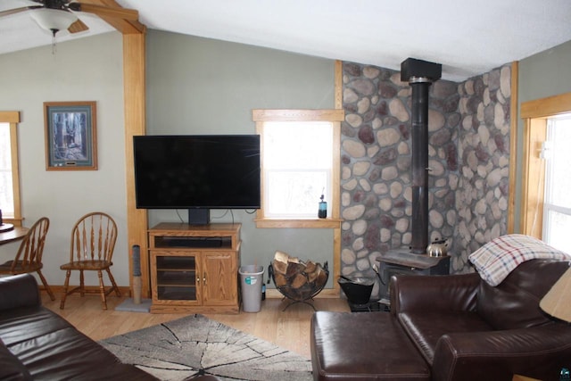 living area with ceiling fan, baseboards, lofted ceiling, a wood stove, and wood finished floors