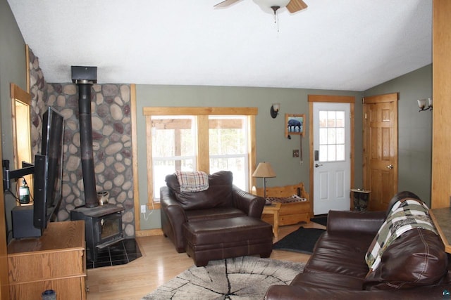 living area with vaulted ceiling, a wood stove, a ceiling fan, and wood finished floors