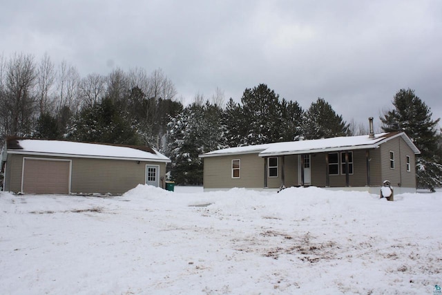 snow covered rear of property featuring a detached garage and an outbuilding