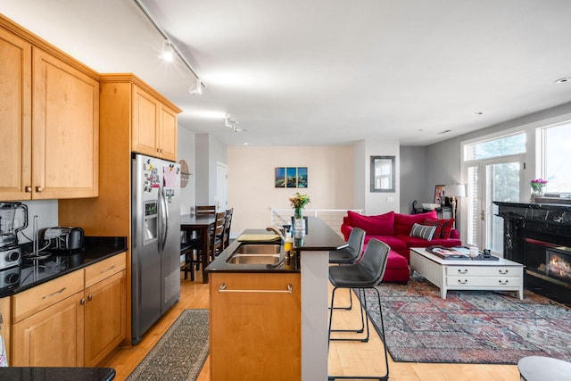 kitchen with dark countertops, an island with sink, light wood-style flooring, stainless steel fridge, and a sink