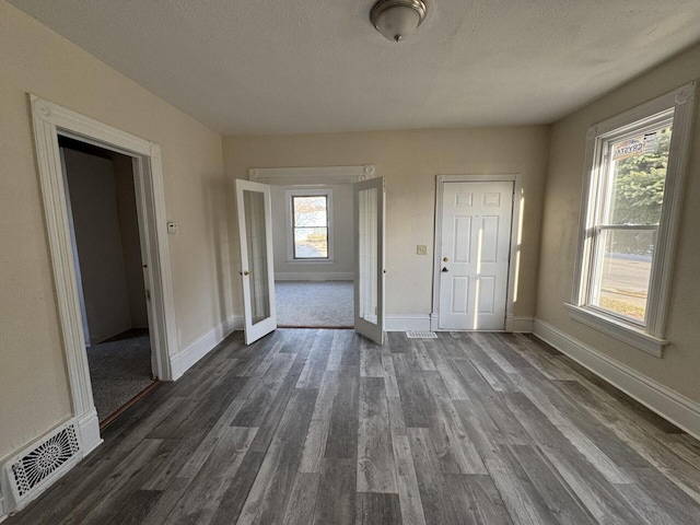 interior space featuring visible vents, baseboards, a textured ceiling, and dark wood-style floors