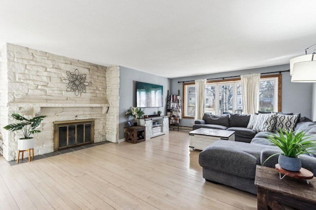 living room featuring a baseboard heating unit, a stone fireplace, and wood finished floors