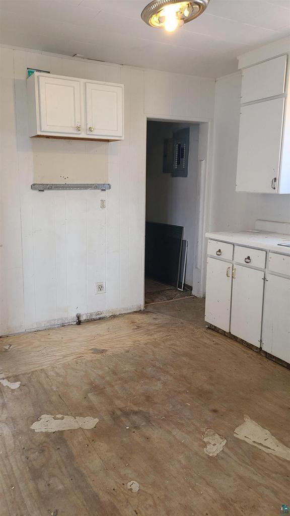 kitchen featuring electric panel, white cabinetry, light countertops, and wood finished floors