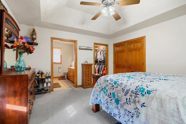 bedroom with a spacious closet, light carpet, a closet, ensuite bath, and a raised ceiling