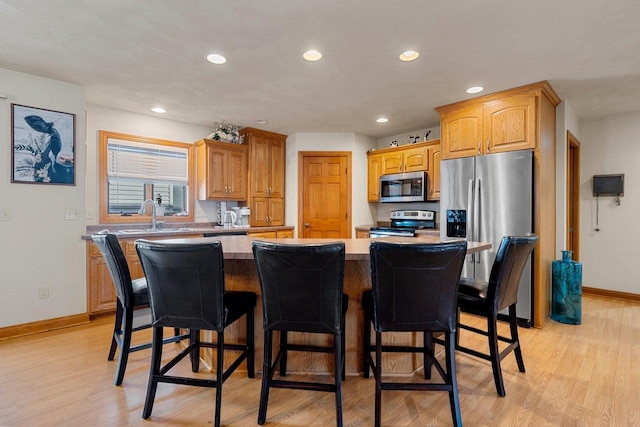 kitchen with a sink, a kitchen island, appliances with stainless steel finishes, and light wood-style flooring